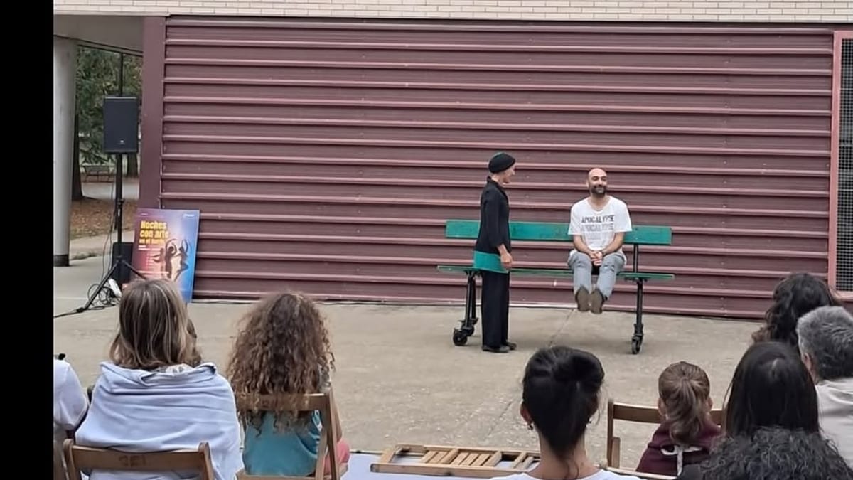 Escena de la obra 'De paseo' durante la actuación en el barrio de San Antonio, con público sentado y actores en escena