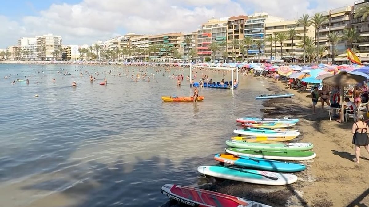 Playa de Torrevieja con bandera azul, arena y mar turquesa bajo cielo despejado