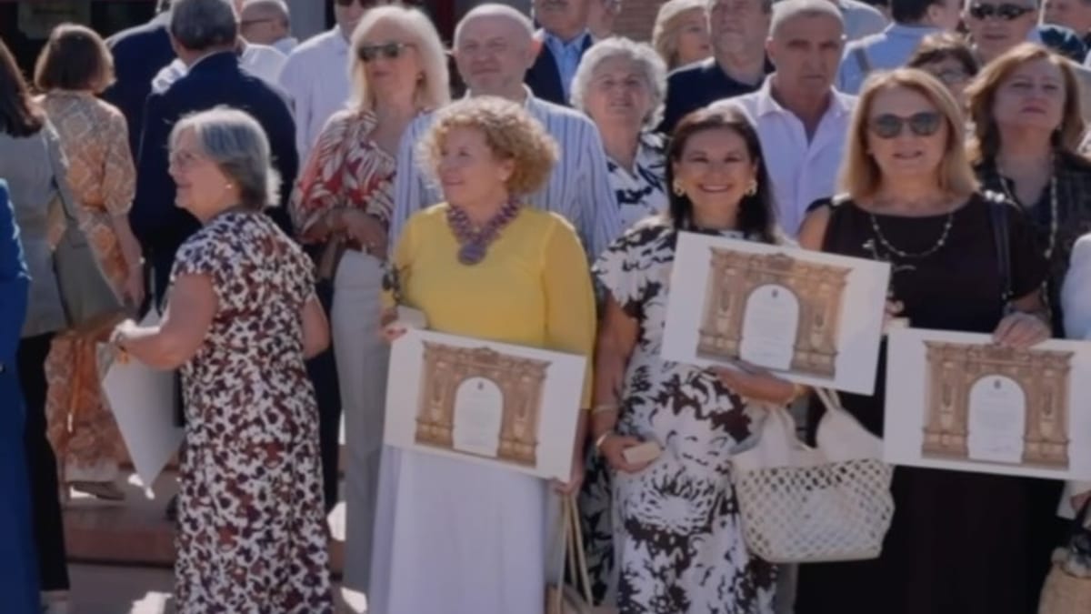 Grupo de personas en un acto de homenaje frente a un edificio municipal con columnas y ladrillo rojo