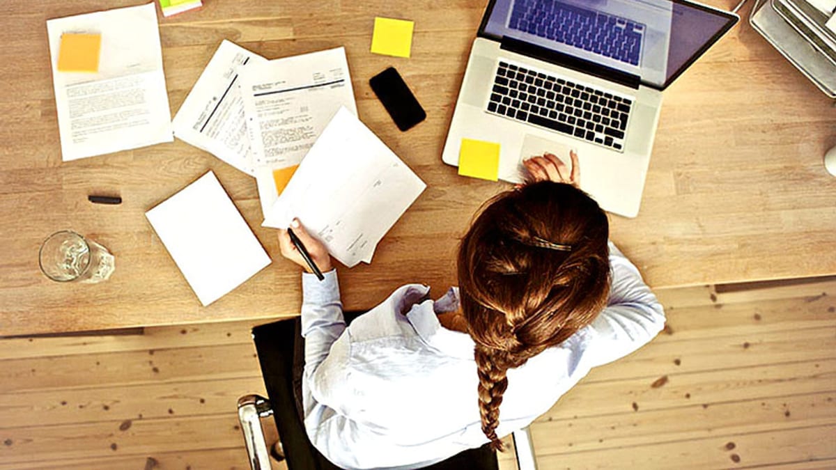 Persona trabajando en un escritorio con ordenador portátil, documentos y notas adhesivas amarillas