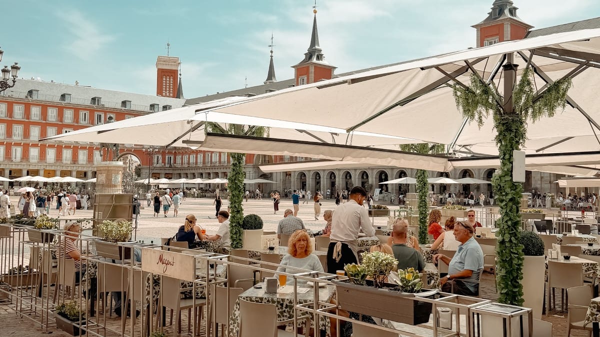 Vista de una terraza en la Plaza Mayor de Madrid con clientes disfrutando de la atmósfera urbana y observando el movimiento de la ciudad