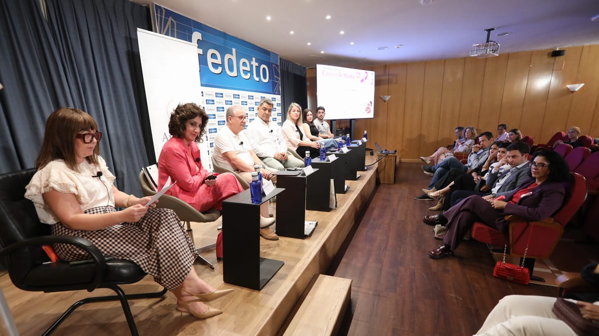 Evento de sensibilización sobre cáncer de mama con panel de participantes en escenario y audiencia, con banner de FEDETO visible