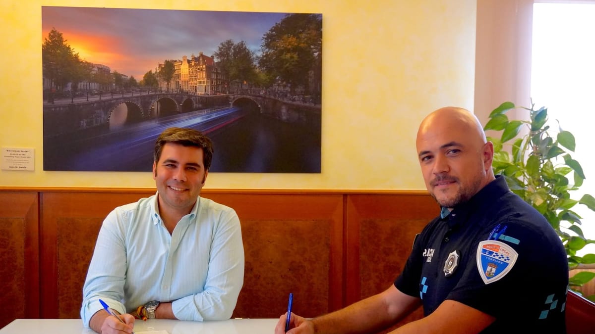 Dos personas firmando documentos en una mesa, tomando posesión del cargo de policía local en Torrijos