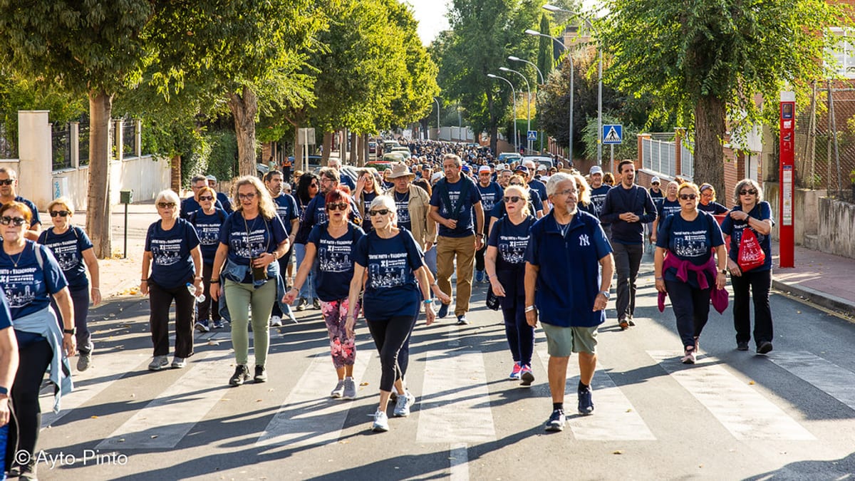 Participantes de la XII Marcha Solidaria Pinto Valdemoro caminando en grupo por una calle arbolada con camisetas azul oscuro