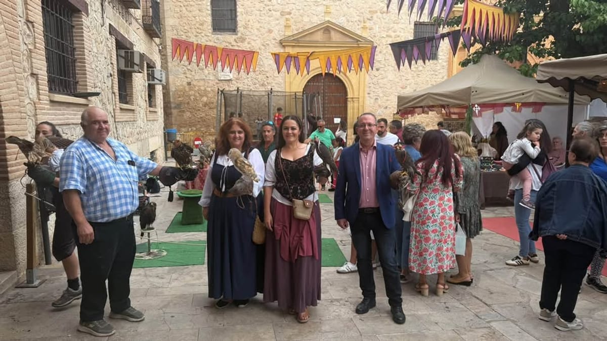 Escena de las XV Jornadas Medievales de Corral de Almaguer con participantes en trajes tradicionales, banderas decorativas y tiendas en el patio del evento